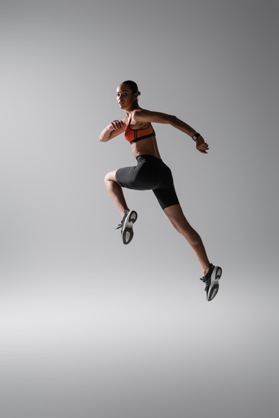 full length of brunette african american woman levitating during work out on grey - Fotoğraf, Görsel