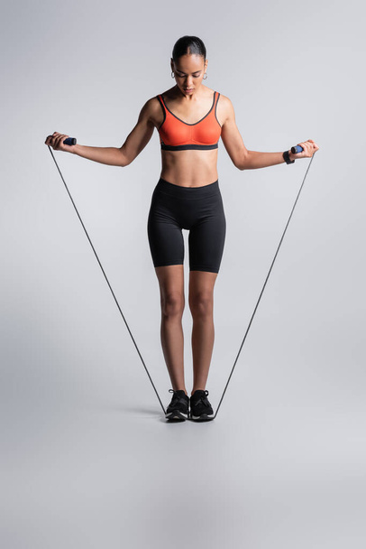full length of sportive african american woman standing with skipping rope on grey  - Foto, Imagen