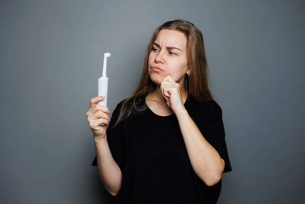 Portrait of a smiling young woman without makeup in a black t-shirt brushing her teeth, mature woman, natural beauty concept. Morning brush for teeth, dental ultrasonic brush. - Foto, imagen