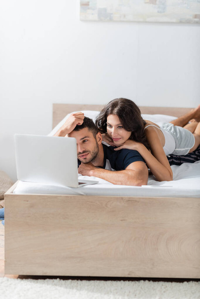 Woman lying on boyfriend near laptop on bed at home  - Photo, image