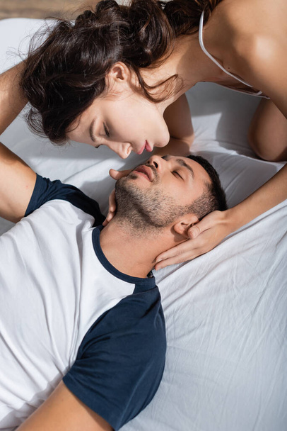 Вид сексапильной женщины, трогающей бойфренда в пижаме на кровати  - Фото, изображение