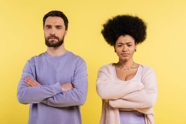 displeased interracial couple standing with crossed arms while looking at camera isolated on yellow - Foto, imagen