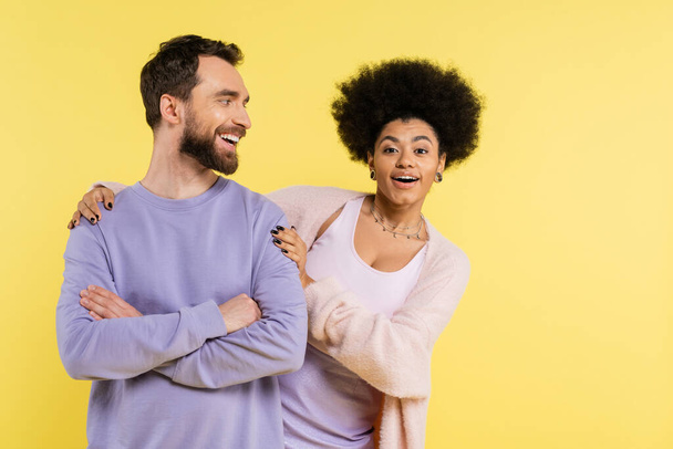 happy and trendy african american woman hugging shoulders of cheerful bearded man isolated on yellow - Foto, imagen