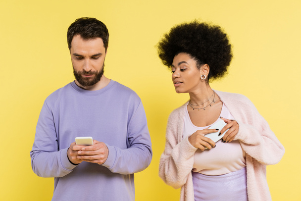 curious african american woman looking at boyfriend messaging on mobile phone isolated on yellow - Fotoğraf, Görsel