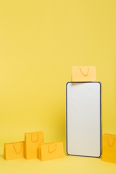vertical view of huge mock-up of smartphone near shopping bags on yellow background - Fotografie, Obrázek