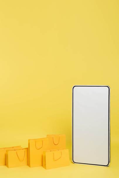 вертикальный вид торговых мешков рядом с огромным шаблоном смартфона на желтом фоне - Фото, изображение