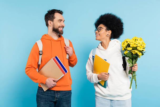 happy african american student with flowers smiling at bearded boyfriend on blue - Photo, image