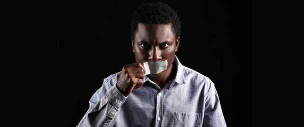 African-American man removing tape from mouth on dark background. Stop racism - Valokuva, kuva
