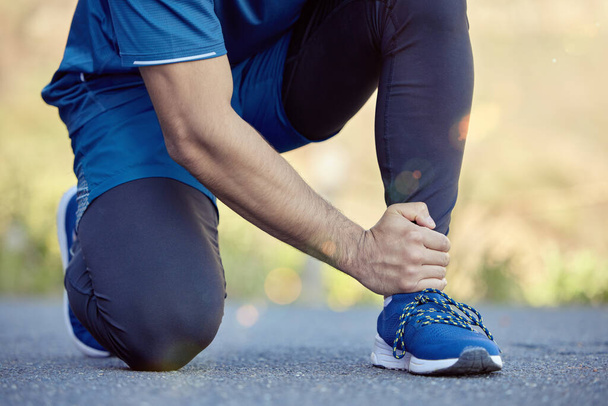 Ankle pain is a result of poor running shoes. an unrecognisable man kneeling and suffering from a sprained ankle during his outdoor workout - Foto, Bild