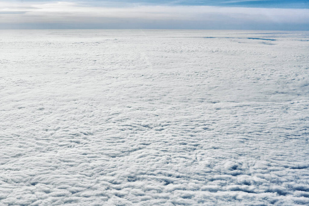 Breathtaking over clouds view from aircraft window, thick white blue clouds looks like soft foam, overcast with fresh frosty air. Beautiful cloudy sky view to troposphere, heavy cloudiness - Zdjęcie, obraz