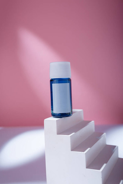 Μπλε μπουκάλι ορού ή οξύ με κενή ετικέτα, δοχείο καλλυντικών φροντίδας mock up template on white concrete stairs, pink background - Φωτογραφία, εικόνα
