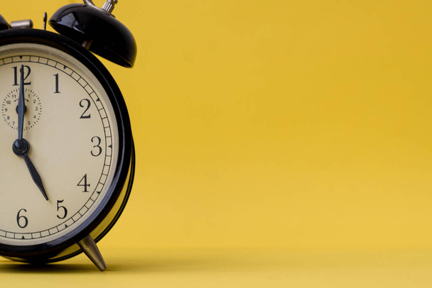Analog alarm clock displaying five o'clock on a yellow background with copy space. Vintage and retro feel. - Foto, afbeelding