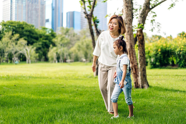 Portrait of happy love asian grandmother and asian little cute girl enjoy relax in summer park.Young girl with their laughing grandparents smiling together.Family and togetherness - Photo, Image