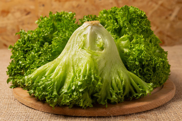 Three bunches of frillis lettuce on a round wooden board, close-up, selective focus - Foto, Imagem