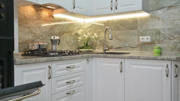 Close-up panning van moderne klassieke luxe witte keuken interieur met magnetron en elektrische ovens, gasfornuis en waterkraan, ovens deuren zijn open - Video