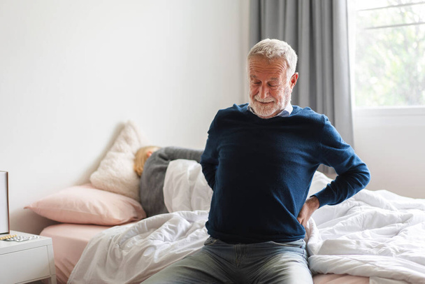 Больной недовольный пожилой мужчина пожилого возраста трогает ее мышечную травму нижней части спины страдает от мышечной боли в спине на home.physical травмы и проблемы со здоровьем - Фото, изображение