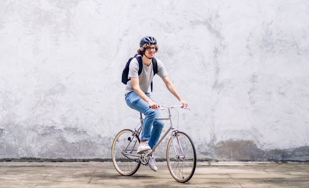 都会の道を自転車で通勤しながらバックパックを楽しみにしているカジュアルなヒップスターハンサムなビジネスマンの肖像が仕事に行きます。ビジネス旅行輸送自転車のコンセプト - 写真・画像