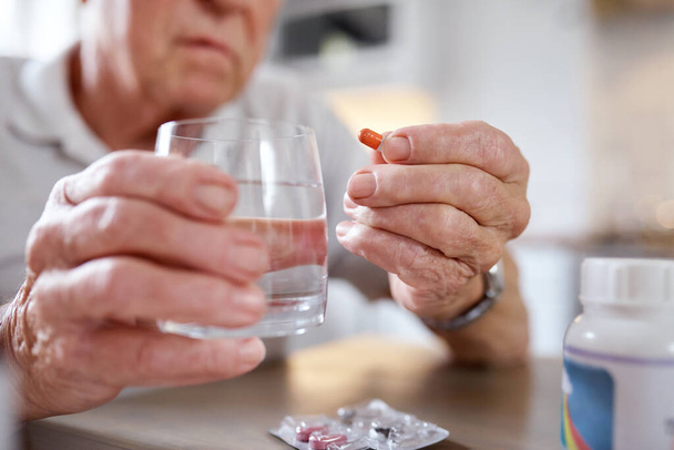 Beware this troubled world, control your intake. Closeup shot of an elderly man taking medication while siting at the kitchen table at home - Photo, image