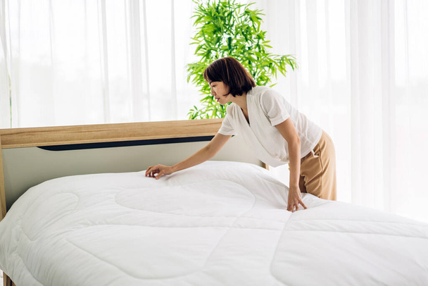 Молодая женщина-домохозяйка убирает кровать и накрывает постельное белье белой чистой простыней. - Фото, изображение