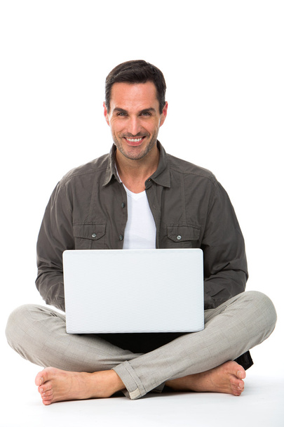 Man sitted on the floor, smiling at camera and working with his laptop - Photo, Image