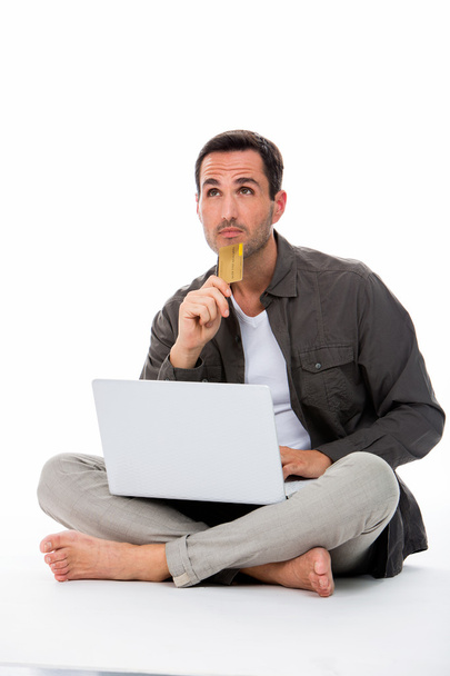 Вдумчивый человек сидел на полу, держа кредитку и покупая онлайн
 - Фото, изображение
