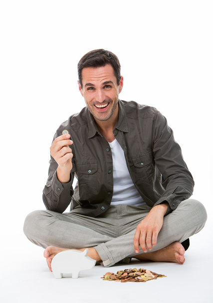 Hombre sentado en el suelo, sonriendo a la cámara, sosteniendo una moneda
 - Foto, imagen