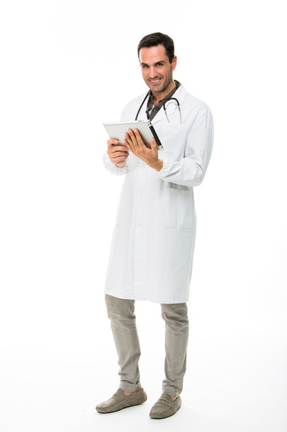 Täyspitkä muotokuva hymyilevä mieslääkäri stetoskoopilla työskennellessään digitaalisen tabletin kanssa
 - Valokuva, kuva