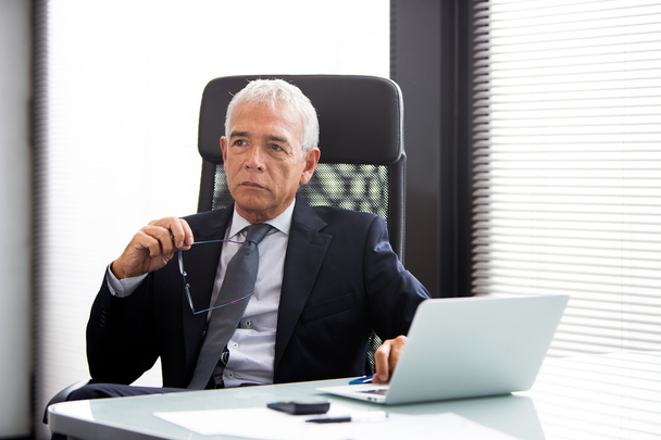 Портрет півдовжини вдумливого бізнесмена в офісі з портативним комп'ютером і тримаючи окуляри
 - Фото, зображення