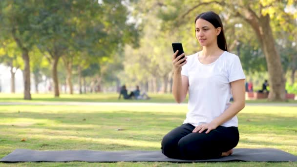 Індійська йога вранці користується мобільним телефоном у парку. - Кадри, відео