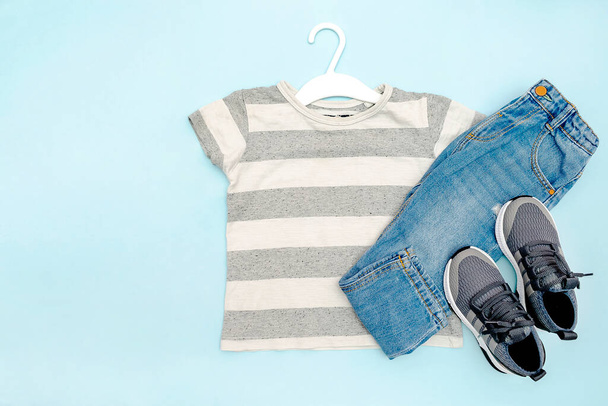 Baby sneakers,t shirt and jeans pants. Set of casual children's clothes and accessories for spring, autumn or summer. Fashion kids outfit,clothing on blue background. Flat lay, top view, overhead. - Foto, Imagem