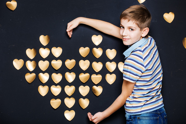 Lachende jongen gouden hart houden op donkere gestructureerde achtergrond - Foto, afbeelding