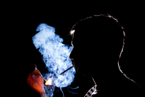 Silhouette of man who lights the cigarette in the dark - 写真・画像
