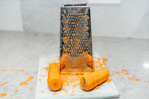 Image of a grated carrot and a grater with peelings sprinkled around. Lived-in Interior with mess, real authentic life, reality, true life. Healthy organic food. - Photo, image