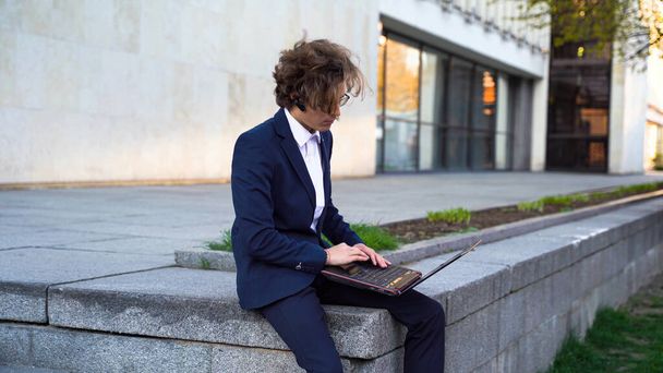 Mladý podnikatel sedí venku na ulici a píše na notebook. Student sedí na univerzitě a píše na počítači. Kancelářský pracovník s laptopem v parku. Kvalitní fotografie - Fotografie, Obrázek
