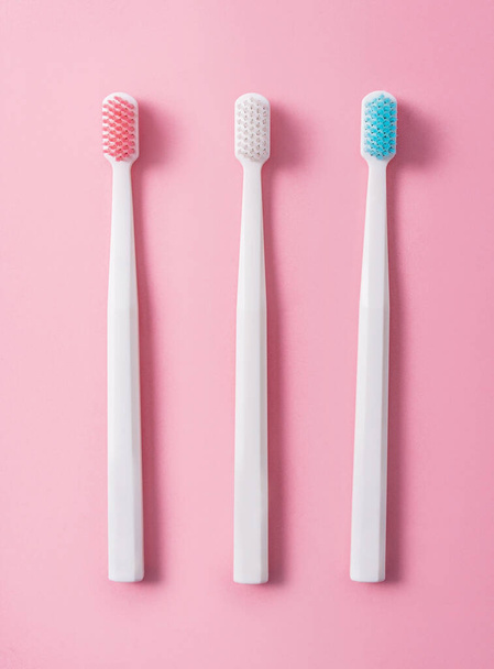 Three plastic toothbrushes on a pink background in pastel colors. Flat lay, top view. - Fotoğraf, Görsel