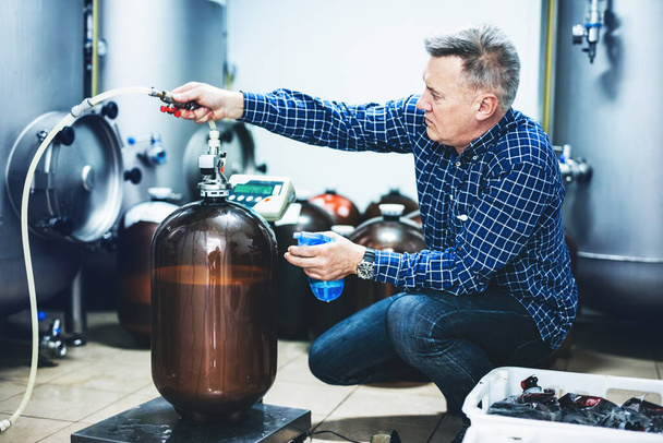 Man working with brewery equipment producing craft beer. Middle-aged man with expertise - Foto, Imagem