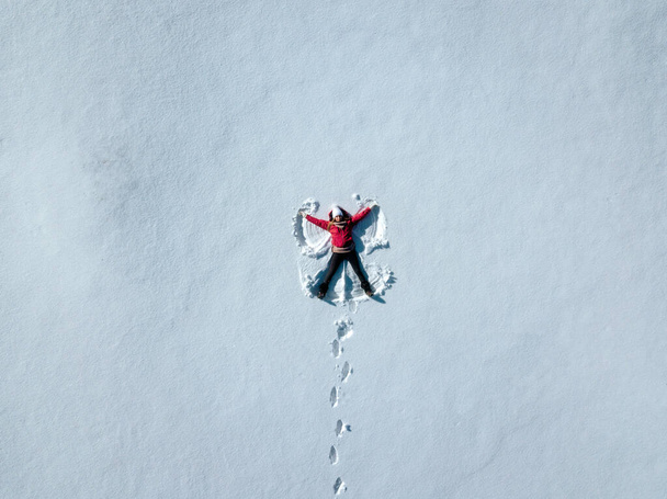 Повітряний знімок жінки в снігу робить сніговий ангел. Жінка лежить у снігу. копіювати текст простору
. - Фото, зображення