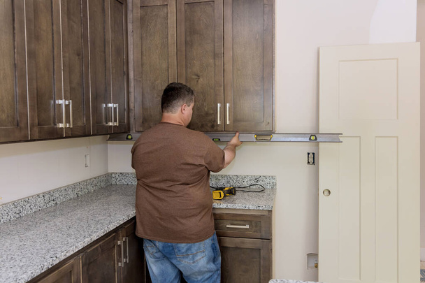 In order to level out installation of brand new kitchen cabinets furniture sets worker hangs level - Photo, image