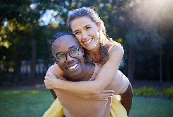 Piggyback, portrait and happy couple in park for wellness in nature, interracial love and support in summer. Excited, freedom and smile black man with woman or people having fun together for a date. - Valokuva, kuva