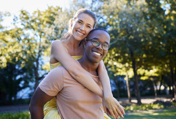 Interracial couple, love and portrait of people with support, care and smile on a summer park adventure. Piggyback, hug and young man and woman outdoor on date together happy about bonding in nature. - Valokuva, kuva