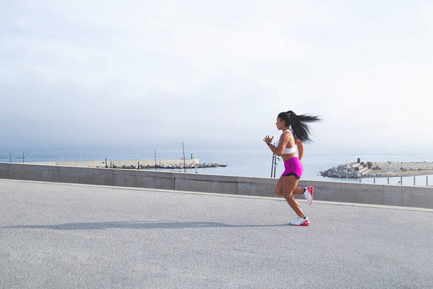 Image of a woman in sportswear jogging in the port. Mixed race outdoor runner. Active lifestyle concept - Foto, Imagen