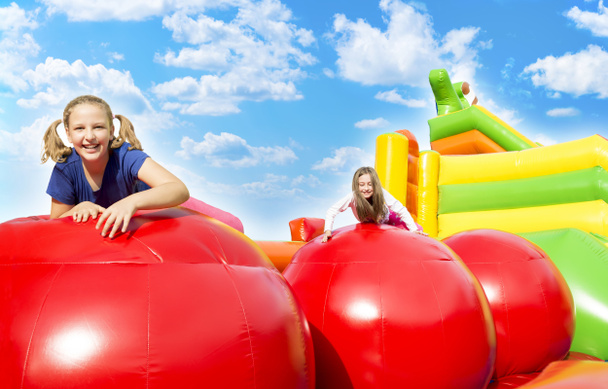 Happy little girls having lots of fun while jumping from ball to ball on an inflate castle on a sunny day outside. - Foto, immagini