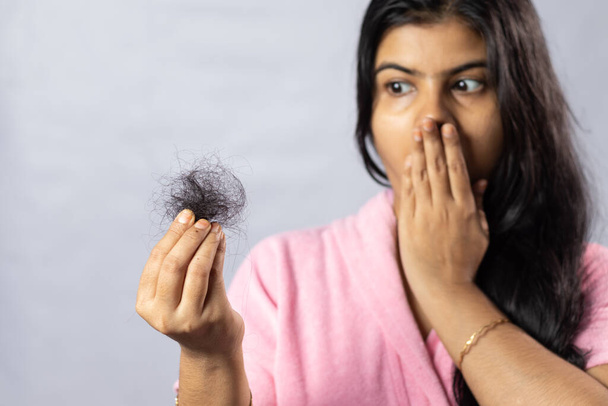 Enfoque selectivo en el cabello caído sostenido en la mano por una mujer india preocupada sobre fondo blanco - Foto, Imagen