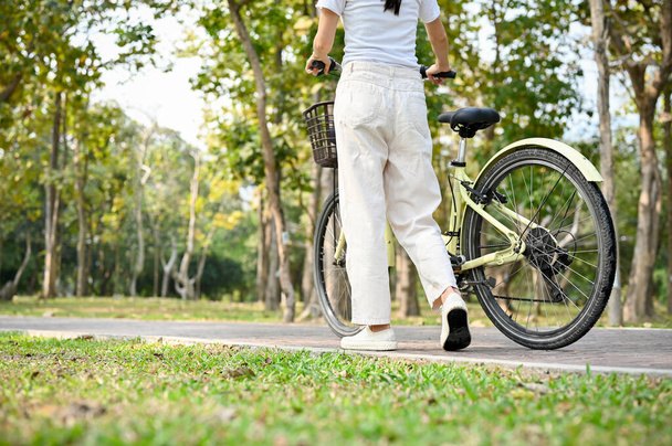 Relaxed young Asian woman walking along the sidewalk with her bicycle in the beautiful nature park. cropped image - Foto, Imagem