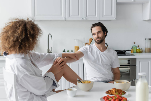 кудрявая женщина соблазняет бородатого парня во время завтрака на кухне  - Фото, изображение