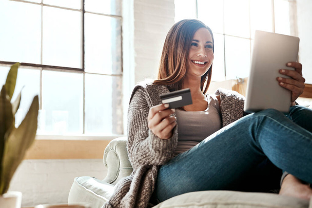 オンラインショッピング、クレジットカード、ソファの上にデジタルタブレットを持つ女性は、オンラインで予約を確認しながらリラックスして笑顔。電子商取引、銀行、クレジットスコアまたはリビングルームでのサブスクリプションのための女の子とカード. - 写真・画像