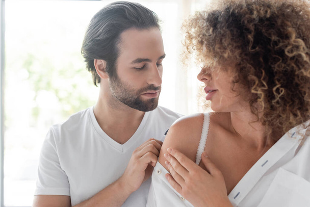 passionate man undressing curly and sensual woman in white shirt in kitchen  - Φωτογραφία, εικόνα