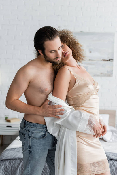 shirtless man in jeans standing with seductive woman in night dress and silk robe  - Fotó, kép