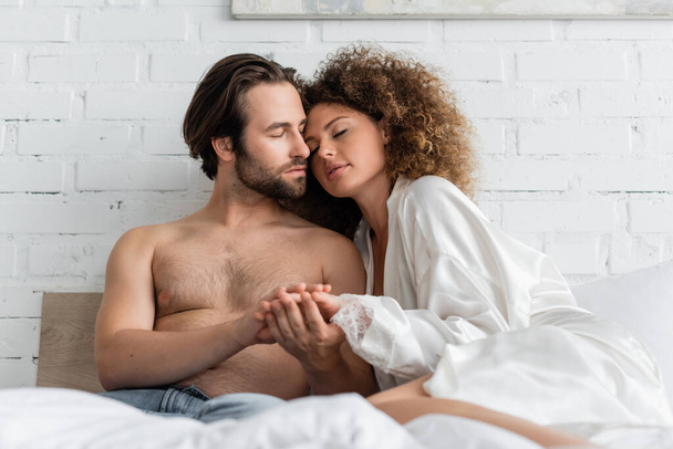 young and sexy couple with closed eyes holding hands while resting in bed  - Foto, imagen