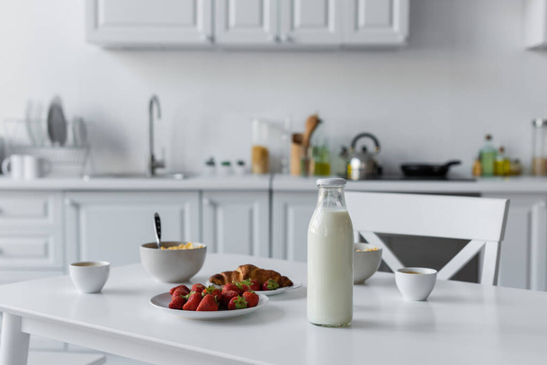 glass bottle with milk near tasty breakfast on table in kitchen  - Foto, Bild